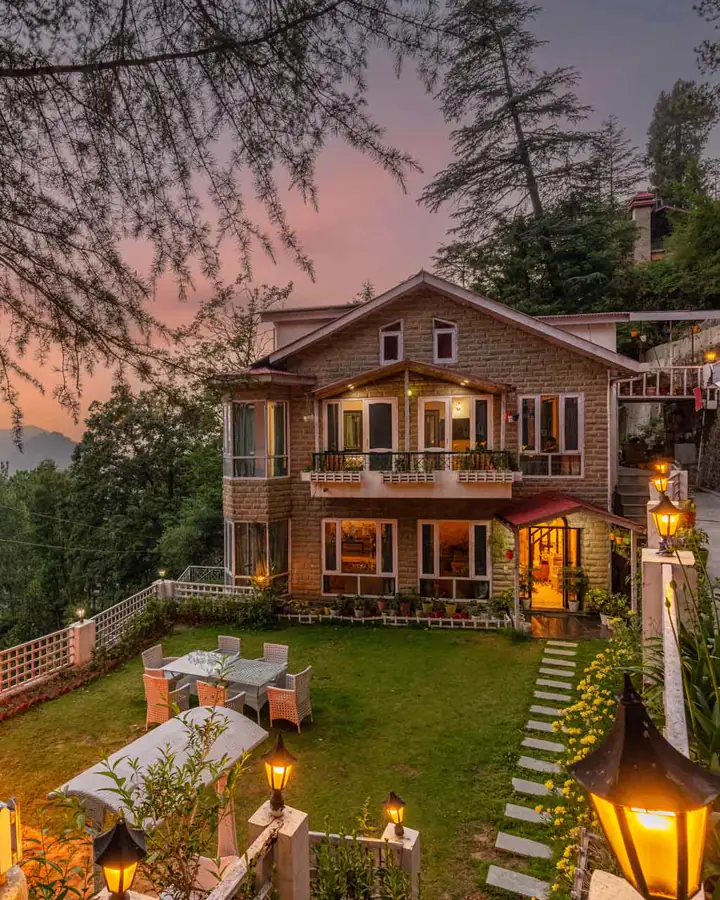 Stone guesthouse with a lit garden on a forested hillside at dusk