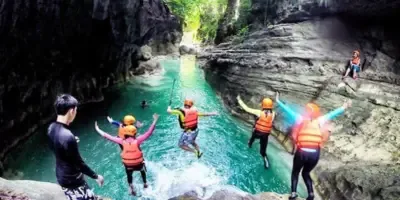 Travellers in life jackets jumping into a turquoise canyon pool